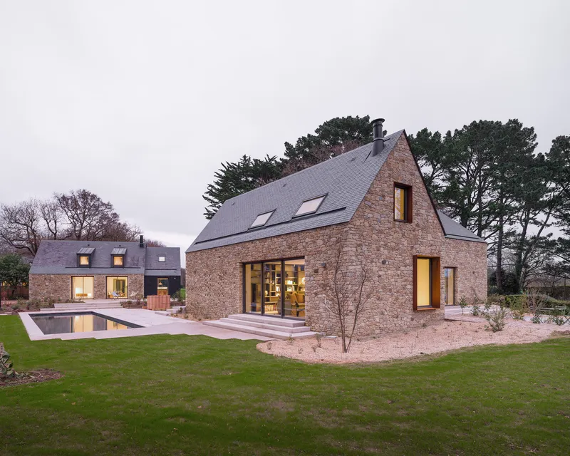 Garden view of the stone facades with lap pool and terrace at twilight