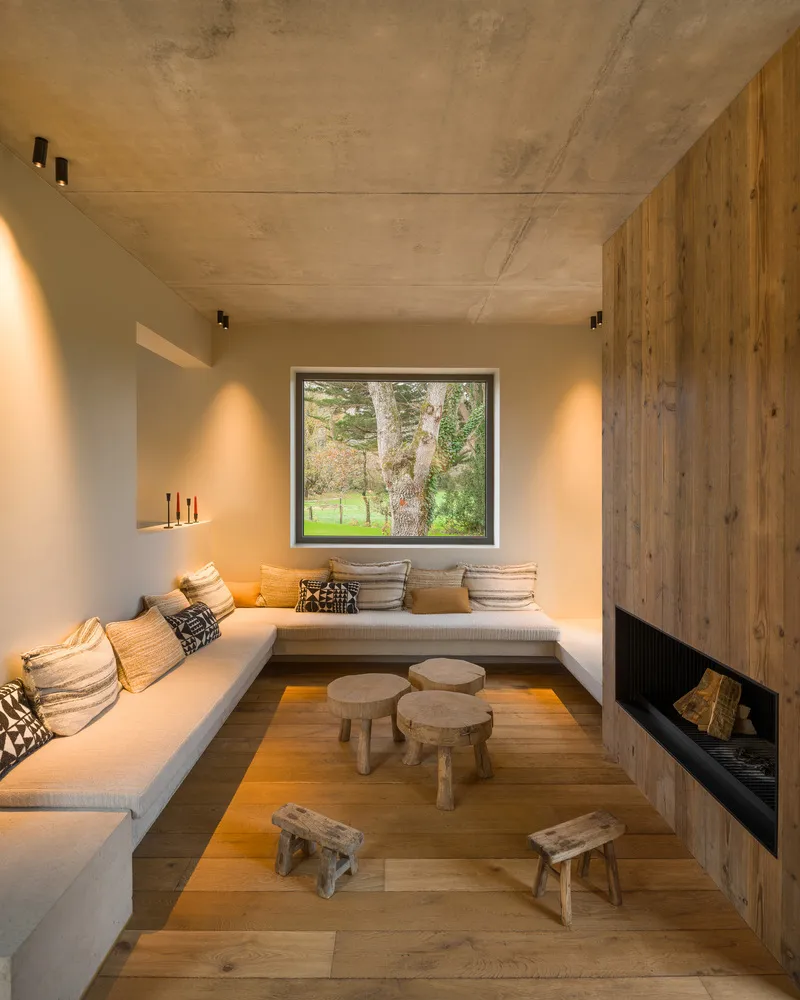 Sunken seating nook with built-in benches, timber fireplace wall and window framing a tree outside