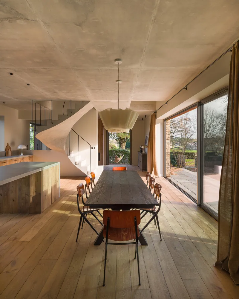 Dining room with exposed concrete ceiling, timber floor and sculptural pendant light above the table