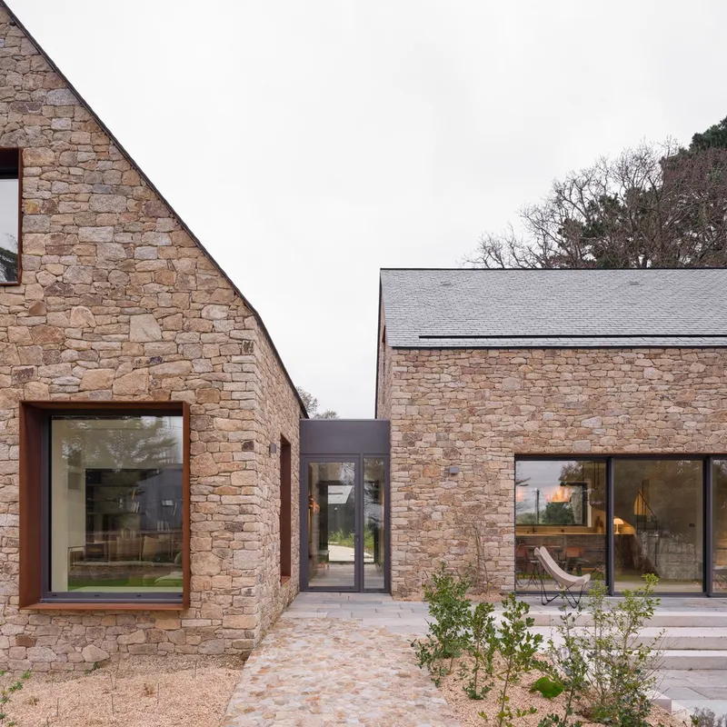 Glazed link passage connecting two stone gable volumes across a gravel courtyard