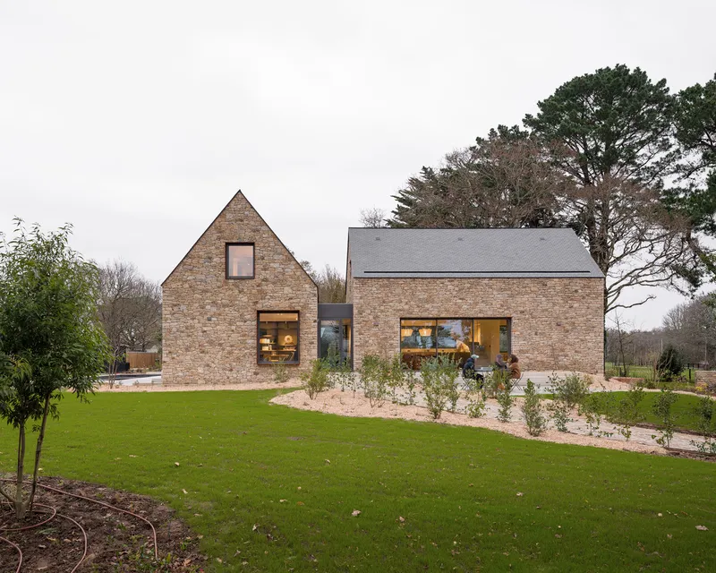 Two-volume brick residence with gabled forms and slate roofs across a lawn under overcast skies
