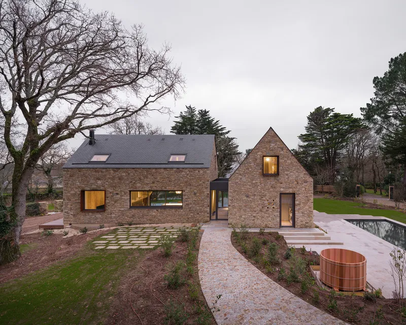Garden view showing the linked brick volumes with gravel paths and a copper soaking tub at dusk