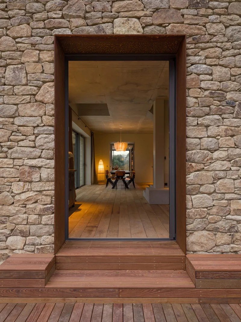 Recessed timber-framed entry through coursed stone wall with view into the lit interior corridor