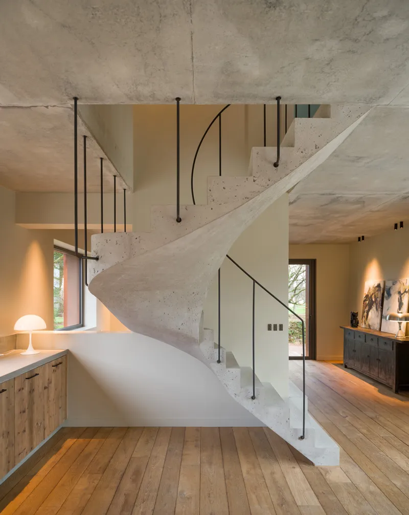 Cast concrete staircase with black steel handrails and glass balustrade rising through the double-height space