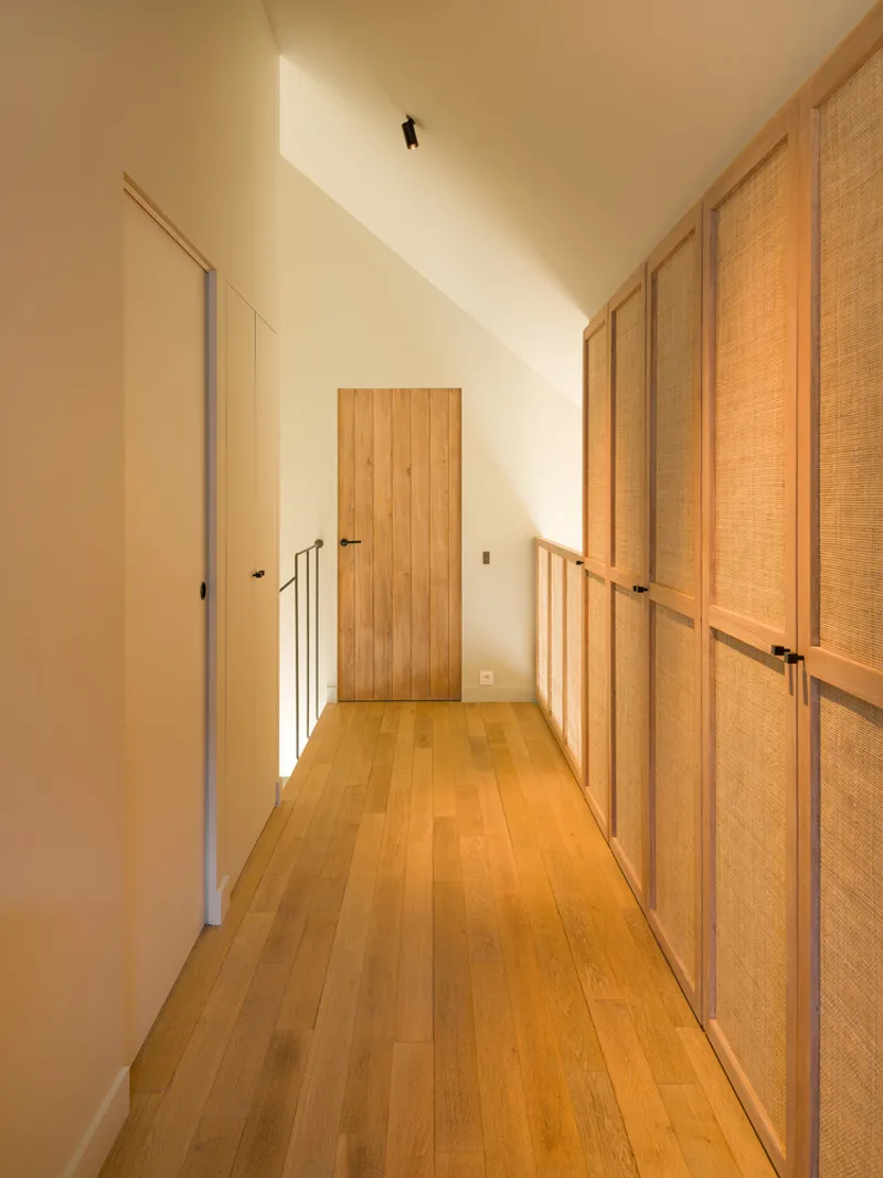 Upper hallway with vaulted ceiling, timber-clad door and cane-paneled closet wall in warm afternoon light