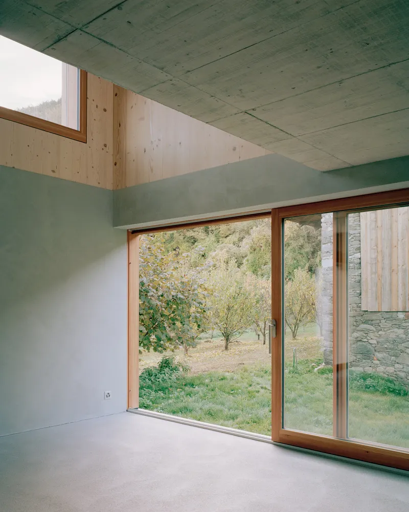 Interior corner with timber-framed sliding doors overlooking an orchard through concrete walls