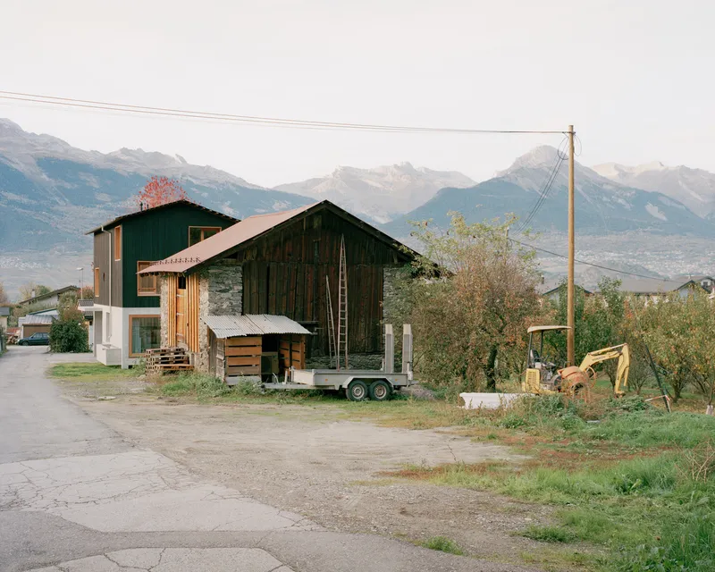 Existing barn structure with corrugated metal siding and a trailer parked alongside in an alpine valley
