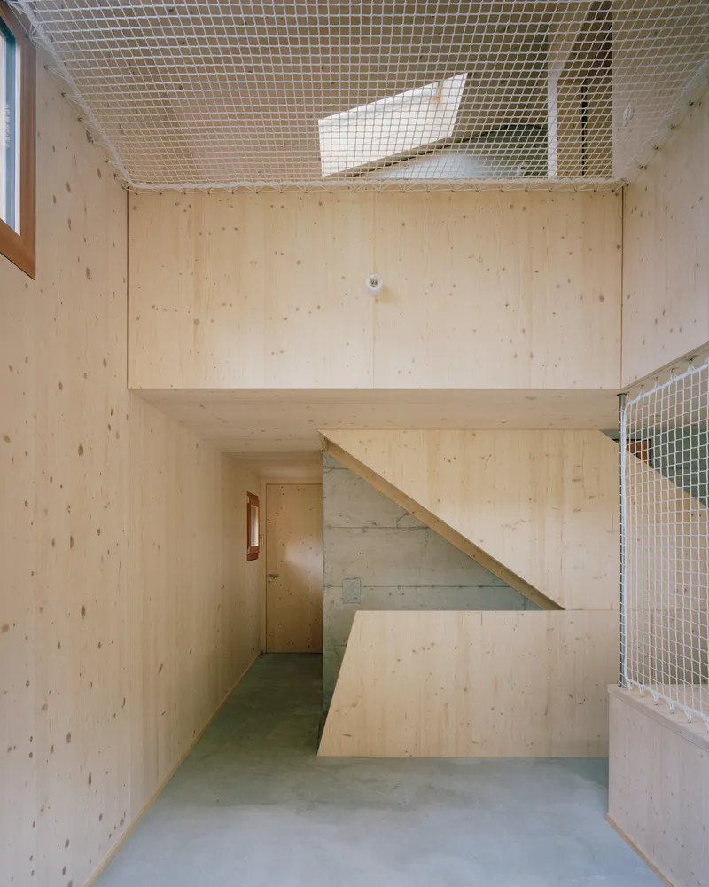 Double-height interior with plywood walls, an angular stair and wire mesh guardrail under a skylight