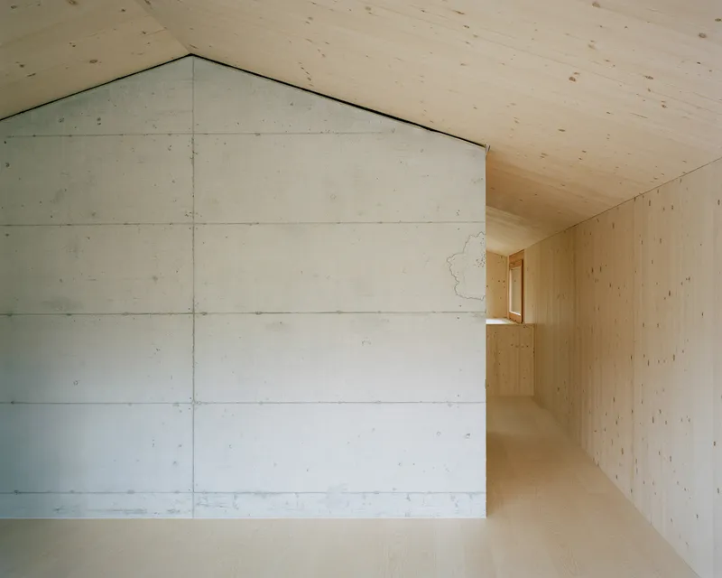 Gabled concrete wall at the end of a corridor lined with pale wood paneling