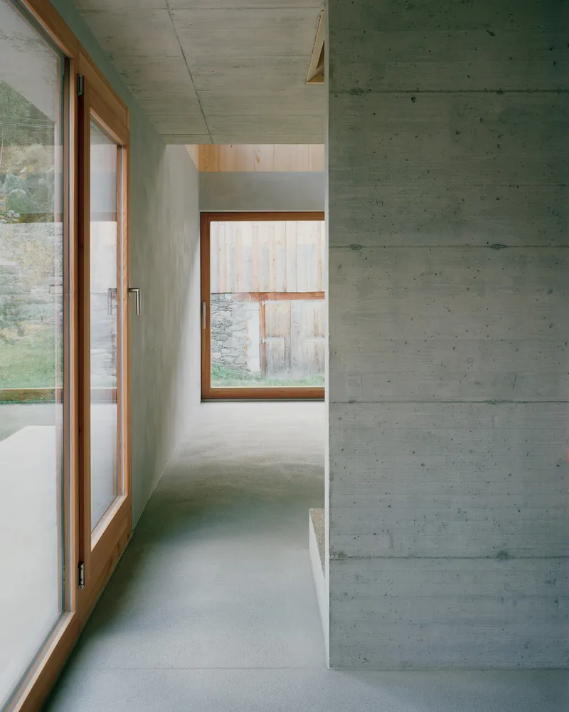 Interior corridor with board-formed concrete walls and timber-framed windows overlooking a grassy slope