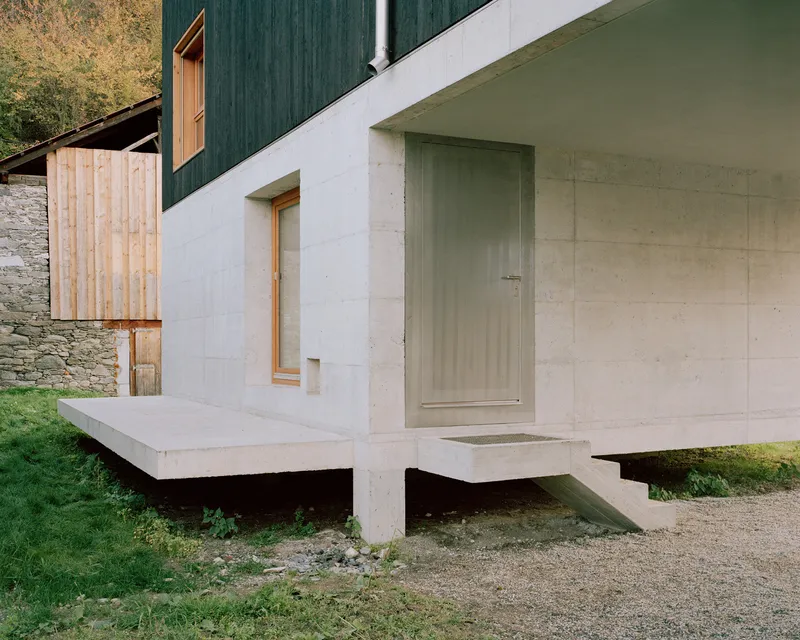 Cantilevered concrete entry platform and steps leading to a light timber window and pale door