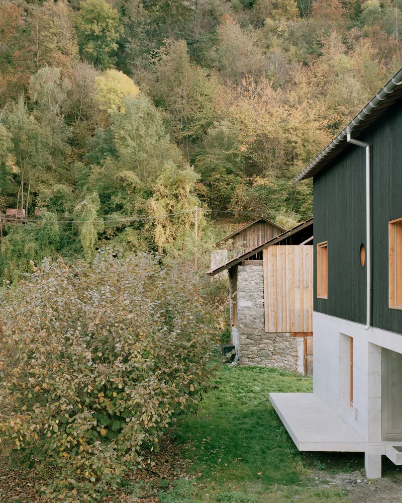 Concrete overhang at the corner of the green timber facade next to an older timber barn