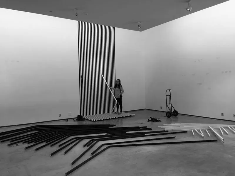 Installation in progress with person assembling black and white striped elements in an empty gallery space
