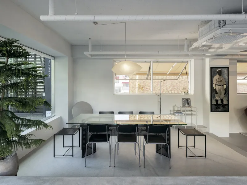 White-walled dining area with exposed ductwork and glass dining table below a clerestory window