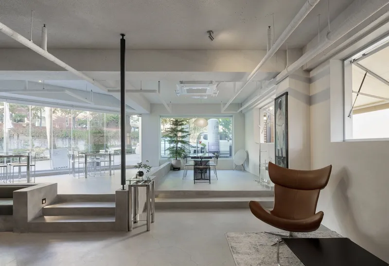 Split-level interior with raised platform, exposed ceiling beams, and glazed wall facing a planted courtyard