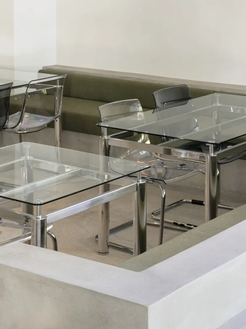 Glass-topped dining table with chrome legs and transparent chairs set into a recessed concrete floor
