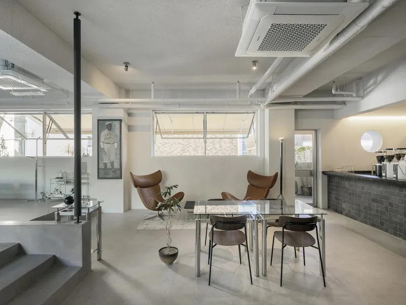 Open-plan interior with suspended column, exposed ducts, and brown leather lounge chairs near the dining zone