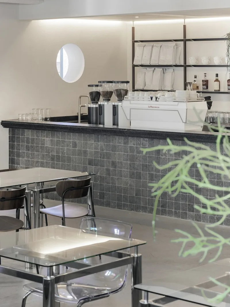 Coffee bar counter clad in dark grey tile with espresso machine and open shelving above