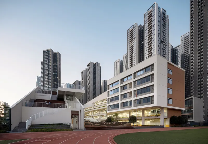 Running track bordering multi-level school building surrounded by residential towers at dusk