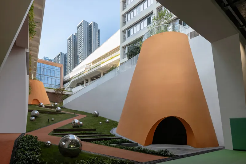 Terraced lawn with conical orange volumes and metal sphere sculptures in courtyard