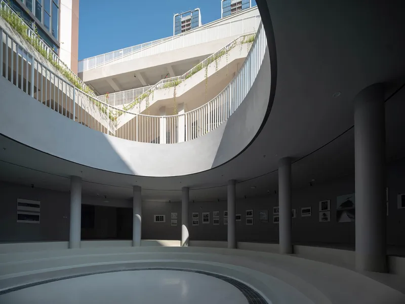 Looking up through a circular atrium with vertical white louvers and planted terraces above