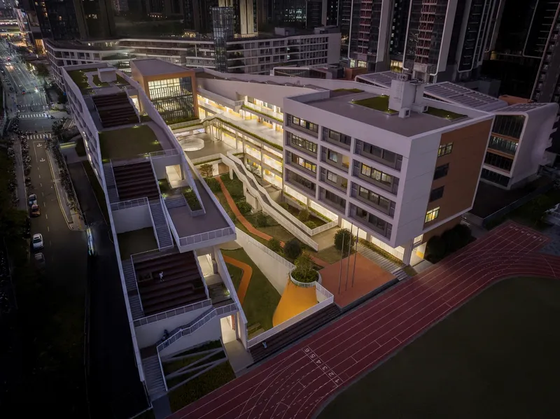 Aerial view at dusk of the illuminated white complex with courtyard gardens and paved plaza