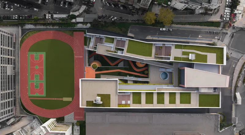 Drone view of the roofscape showing green courtyards and a running track adjacent to the street