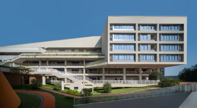 Elevated classroom block supported on concrete columns above landscaped ground level under a clear sky