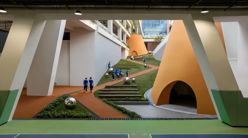 Interior courtyard with grassed slope and orange tunnel beneath white angular walls with students walking