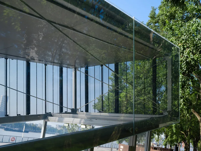 Translucent mesh panels and glass canopy reflecting tree shadows in bright daylight