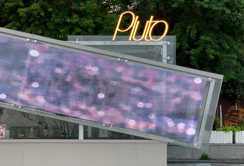Angled mesh screen displaying pink and purple light projection with neon lettering above