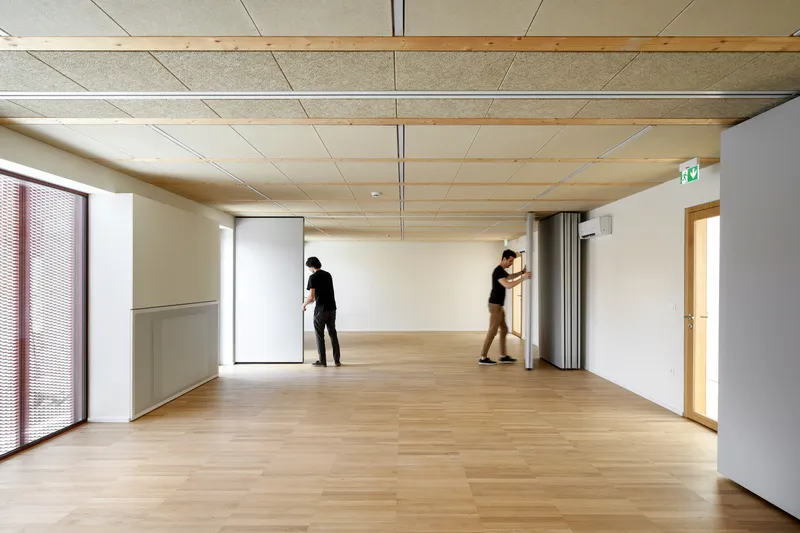 Interior room with timber ceiling panels and blonde wood flooring as two people adjust partitions