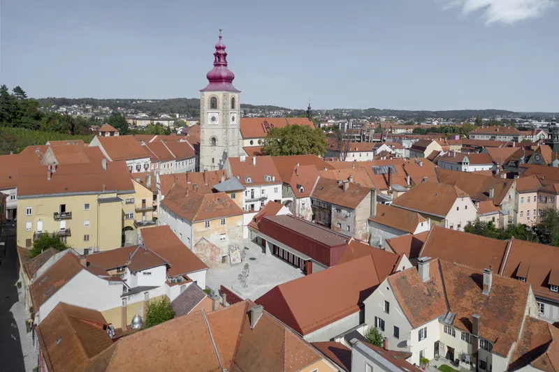 Aerial view of red-tiled rooftops clustered around a white church tower with a pink dome