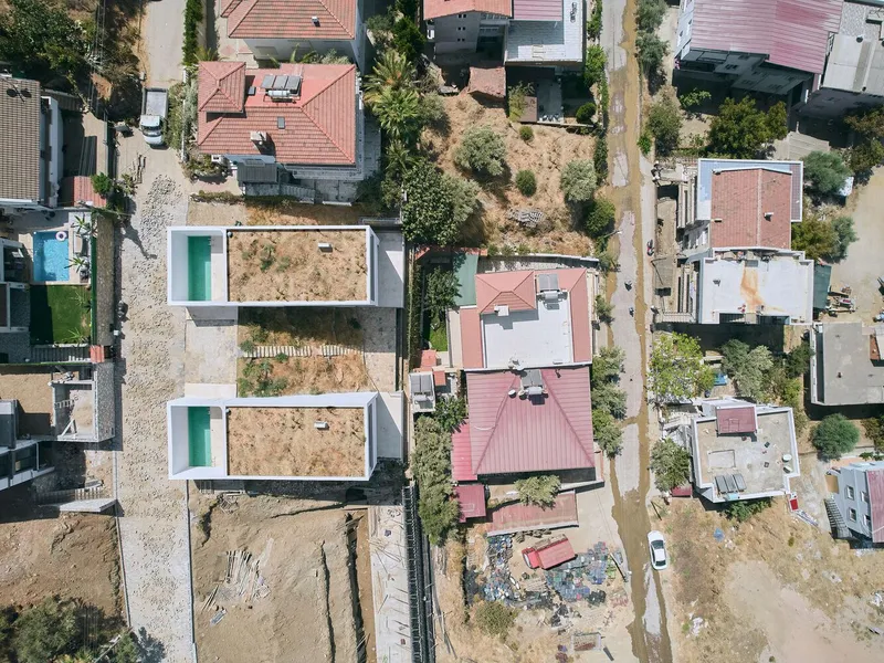 Drone view of paired white rooftop courtyards with turquoise pools among pink-roofed houses
