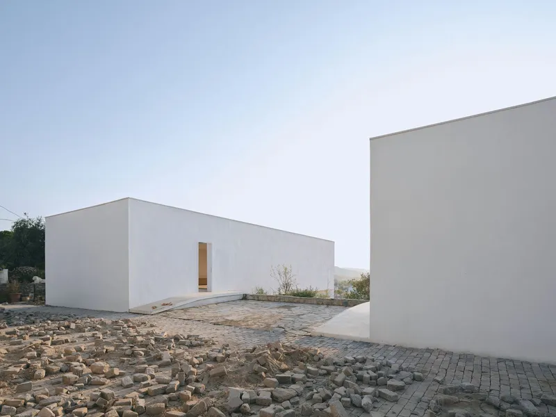 White rendered walls framing a cobblestone courtyard at dusk with single recessed timber doorway