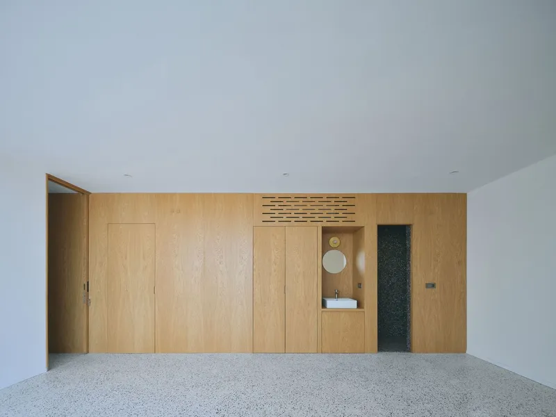 Oak paneled wall with integrated storage and partial view into bathroom through central opening