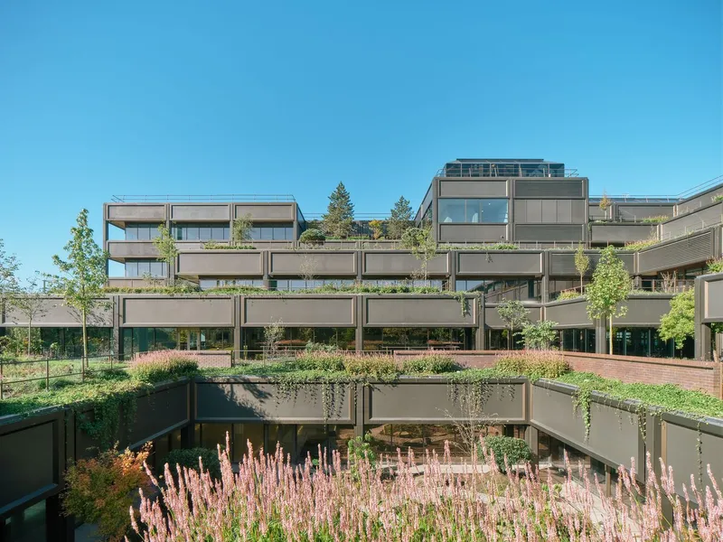 Tiered balconies with integrated planters filled with pink flowering grasses under a clear blue sky