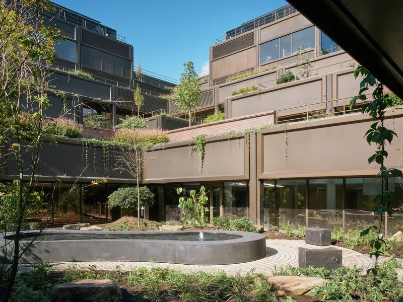 Ground-level courtyard with a circular concrete water feature surrounded by planted beds and young trees
