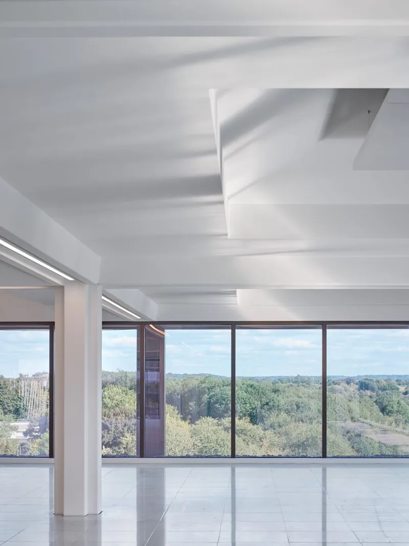 Interior space with white coffered ceiling and floor-to-ceiling windows overlooking a wooded landscape