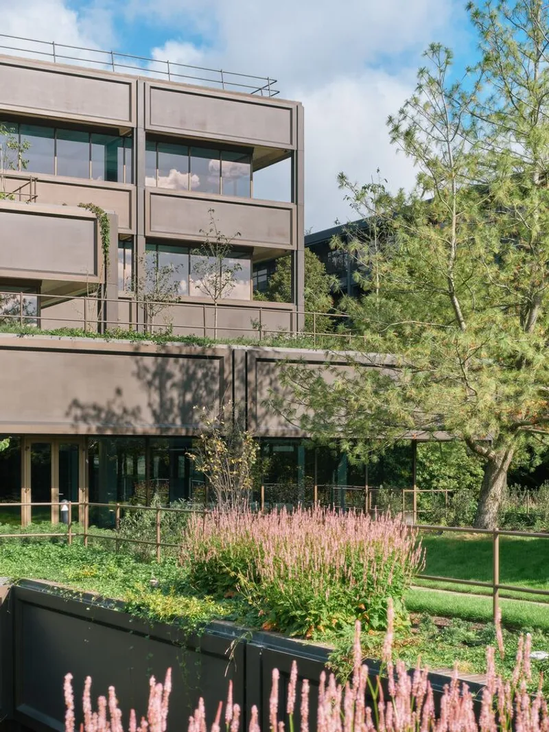 Facade with projecting balconies and planted beds of pink flowering perennials in afternoon sun