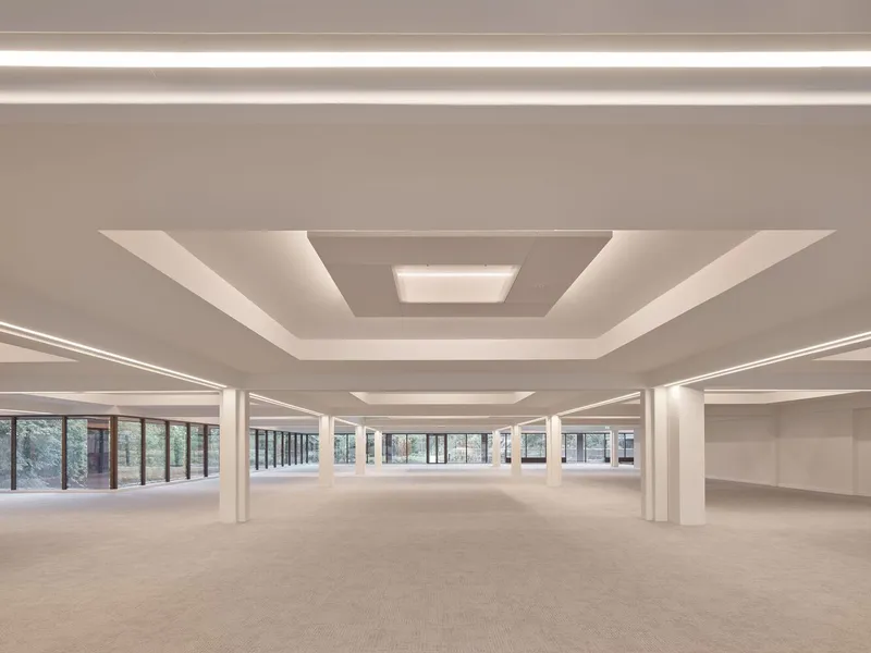 Open-plan interior with white columns, recessed stepped ceiling and continuous band windows along the perimeter