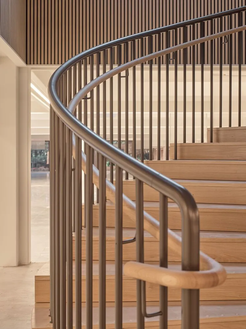 Curved timber stair with bronze metal handrail and vertical wood slat screen in natural light