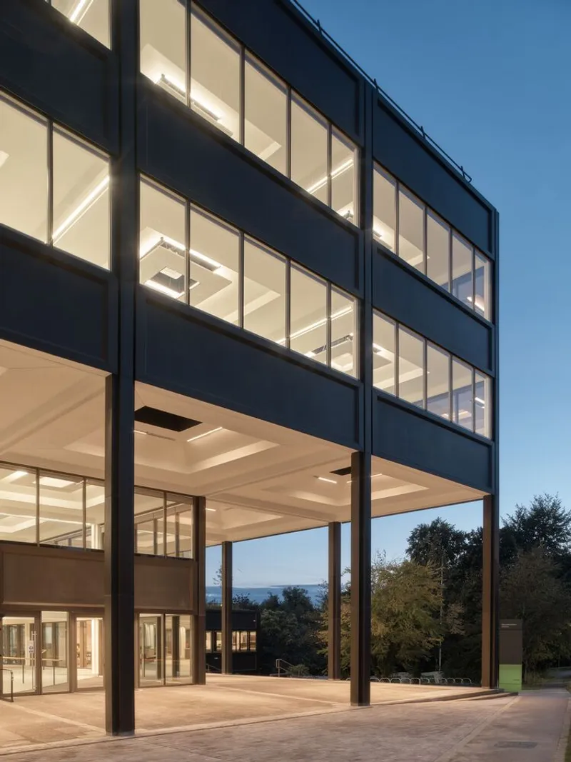 Glass facade with black metal framing and interior lighting visible at dusk