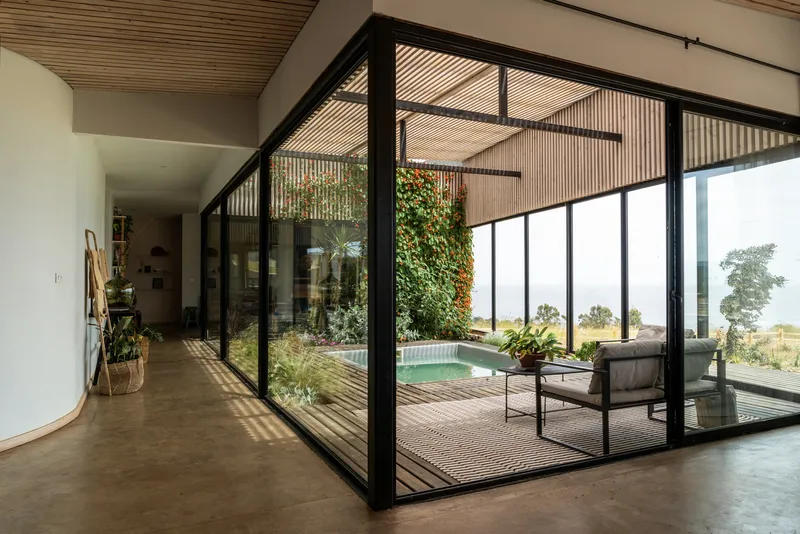 Interior view through black-framed glazing to an enclosed courtyard with pool and vertical greenery