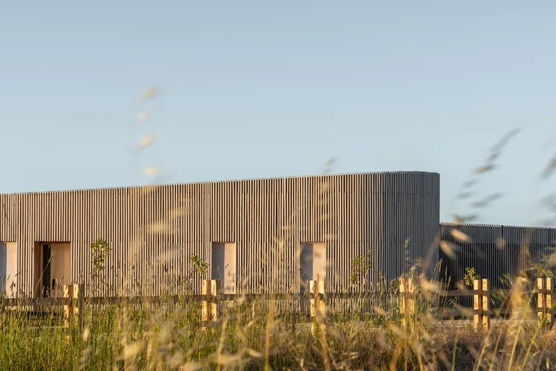 Cylindrical timber volume with vertical slats seen through blurred foreground grasses
