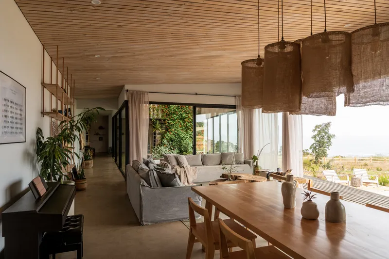 Living space with timber slatted ceiling, woven pendant lights and floor-to-ceiling glazing overlooking landscape
