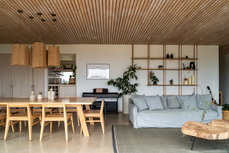 Open living and dining space with timber slatted ceiling and open shelving wall