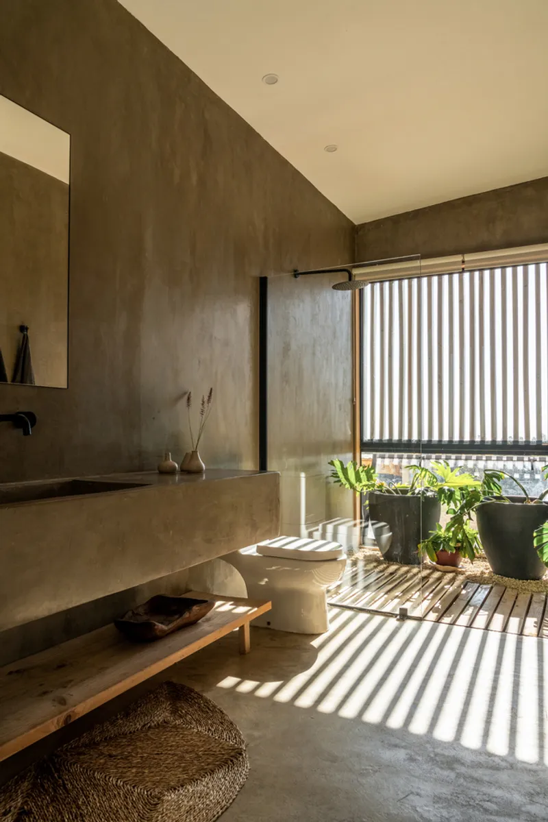 Concrete bathroom with integrated sink and slatted timber screen casting striped shadows across potted plants