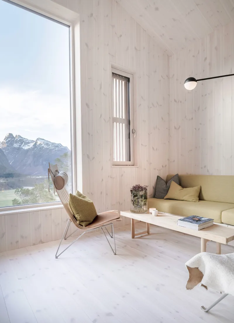 Light-filled living room with pale timber walls and corner window framing distant alpine ridges