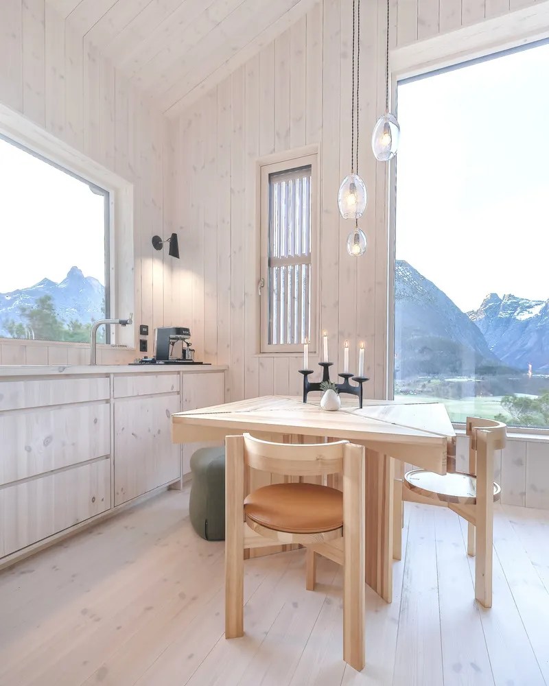 Dining area with timber table and pendant lights overlooking mountains through floor-to-ceiling glazing
